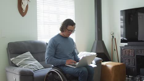 Glücklicher-Kaukasischer-Behinderter-Mann-Im-Rollstuhl,-Der-Laptop-Im-Wohnzimmer-Benutzt