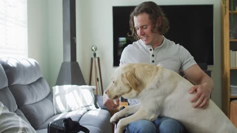 Happy-caucasian-disabled-man-in-wheelchair-playing-with-pet-dog-in-living-room