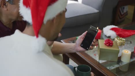 Son-and-father-making-christmas-video-call-on-smartphone-with-blank-screen-and-copy-space-at-home