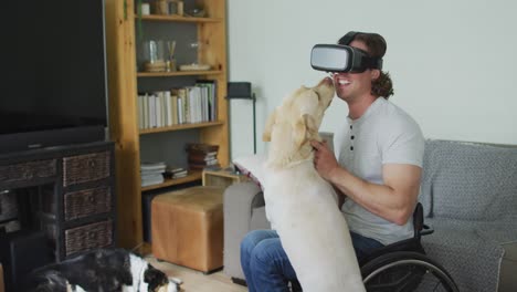 Happy-caucasian-disabled-man-in-wheelchair-wearing-vr-headset-playing-with-pet-dog-in-living-room