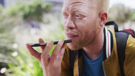 Happy-albino-african-american-man-with-dreadlocks-in-park-talking-on-smartphone