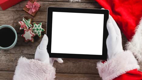 Animation-of-santa-claus-holding-tablet-with-copy-space,-christmas-cookies-in-background