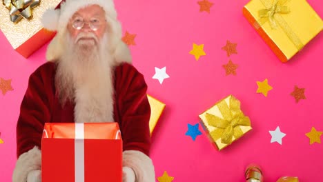 Composition-of-santa-claus-holding-present-on-pink-background-with-christmas-boxes-and-stars