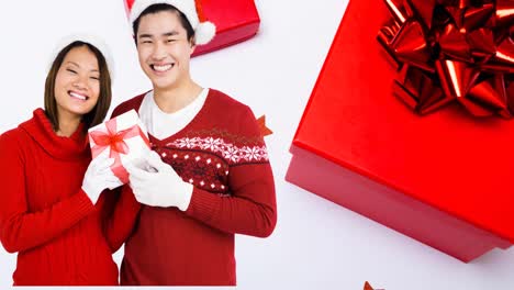 Composition-of-asian-couple-in-santa-hats-holding-christmas-present-on-white-background-with-boxes