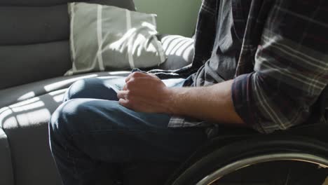 Midsection-of-caucasian-disabled-man-in-wheelchair-holding-cup-of-coffee-in-living-room