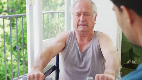Disabled-senior-man-grimacing-while-lifting-dumbbells-with-support-of-male-instructor-at-health-club