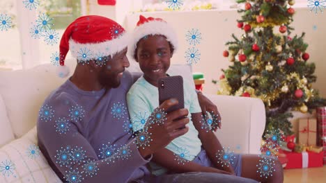 Animation-of-snowflakes-over-african-american-father-and-son-on-christmas-video-call-on-smartphone