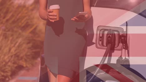 Bandera-De-Gran-Bretaña-Sobre-Una-Mujer-Usando-Un-Teléfono-Inteligente-Y-Cargando-Un-Auto-Eléctrico