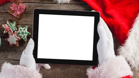 Animation-of-santa-claus-using-tablet-with-copy-space,-christmas-cookies-in-background