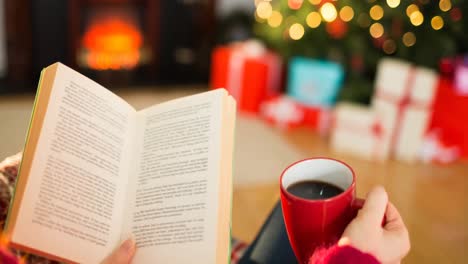 Animation-of-hands-of-caucasian-woman-with-coffee-reading-book-at-christmas-time