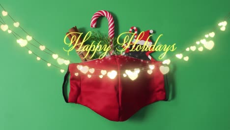 Animation-of-happy-holidays-christmas-text-over-lights-and-face-mask-on-green-background