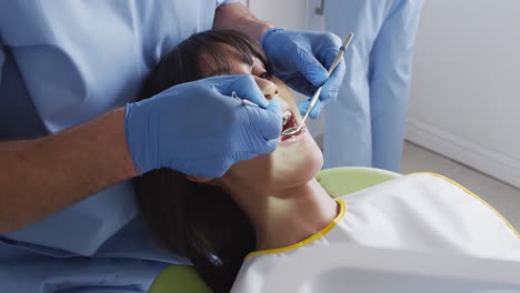 Dentista-Masculino-Caucásico-Y-Enfermera-Dental-Examinando-Los-Dientes-De-Una-Paciente-En-Una-Clínica-Dental-Moderna