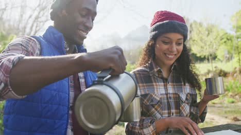 Smiling-diverse-couple-drinking-tea-and-hiking-in-countryside