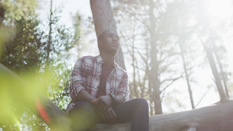 Smiling-african-american-man-sitting-on-tree-during-hiking-in-countryside