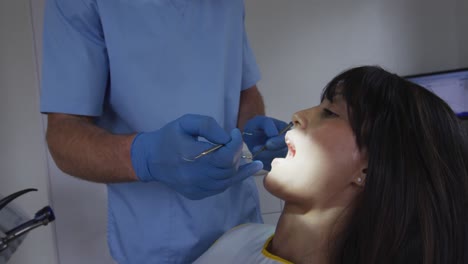 Dentista-Masculino-Caucásico-Examinando-Los-Dientes-De-Una-Paciente-En-Una-Clínica-Dental-Moderna
