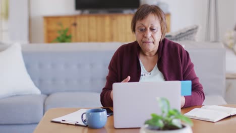 Glückliche-Afroamerikanische-ältere-Frau-Am-Esstisch,-Die-Mit-Dem-Laptop-Einen-Videoanruf-Tätigt-Und-Spricht