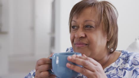 Happy-african-american-senior-woman-enjoying-drinking-cup-of-tea,-looking-away-smiling