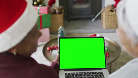 Smiling-senior-diverse-couple-in-santa-hats-making-laptop-christmas-video-call,-with-green-screen