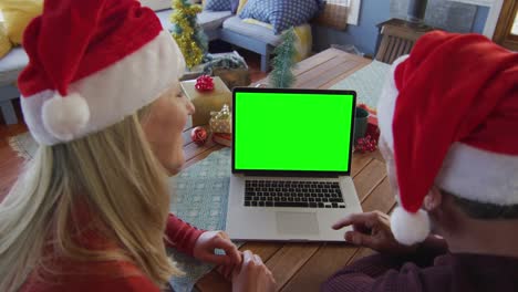 Smiling-caucasian-couple-in-santa-hats-making-laptop-christmas-video-call,-with-green-screen