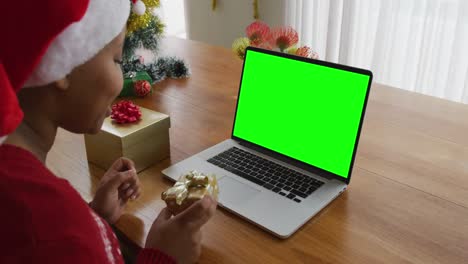 African-american-woman-with-present-making-laptop-christmas-video-call,-with-green-screen-copy-space