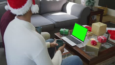 Biracial-father-with-son-in-santa-hats-making-laptop-christmas-video-call,-with-green-screen