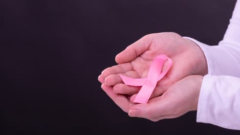 Video-of-hands-of-caucasian-woman-holding-pink-cancer-awareness-ribbon-on-black-background