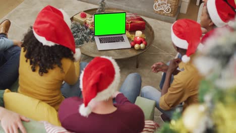 Smiling-diverse-friends-in-santa-hats-making-laptop-christmas-video-call,-with-green-screen