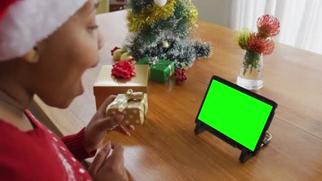 Happy-african-american-woman-with-present-making-laptop-christmas-video-call,-with-green-screen