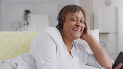 Feliz-Mujer-Mayor-Afroamericana-Usando-Auriculares-Disfrutando-Usando-Un-Teléfono-Inteligente-Y-Sonriendo