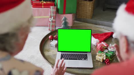 Senior-caucasian-couple-in-santa-hats-making-laptop-christmas-video-call,-with-green-screen