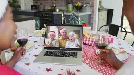 Smiling-african-american-couple-using-laptop-for-christmas-video-call-with-family-on-screen