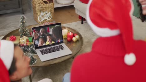 African-american-family-with-santa-hats-using-laptop-for-christmas-video-call-with-family-on-screen
