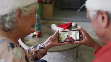 Lächelndes-älteres-Kaukasisches-Paar,-Das-Sein-Smartphone-Für-Einen-Weihnachtsvideoanruf-Mit-Einer-Frau-Auf-Dem-Bildschirm-Nutzt