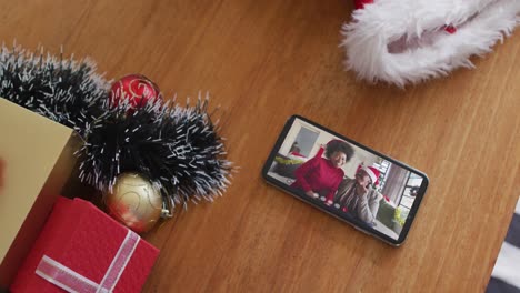 Smiling-african-american-mother-and-daughter-with-santa-hats-on-christmas-video-call-on-smartphone