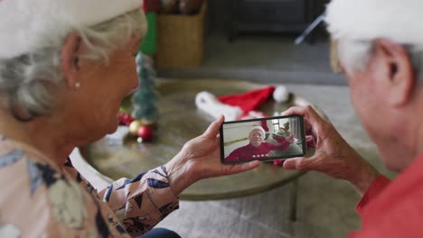 Lächelndes-älteres-Kaukasisches-Paar,-Das-Sein-Smartphone-Für-Einen-Weihnachtsvideoanruf-Mit-Einem-Mann-Auf-Dem-Bildschirm-Nutzt