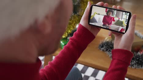 Kaukasischer-Mann-Mit-Weihnachtsmütze-Nutzt-Smartphone-Für-Weihnachtsvideoanruf,-Mit-Frau-Auf-Dem-Bildschirm