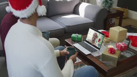 Biracial-father-and-son-using-laptop-for-christmas-video-call-with-smiling-man-on-screen