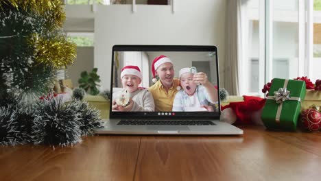 Smiling-caucasian-family-wearing-santa-hats-on-christmas-video-call-on-laptop