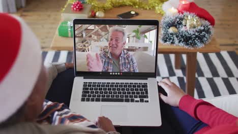 African-american-mother-and-daughter-using-laptop-for-christmas-video-call-with-man-on-screen