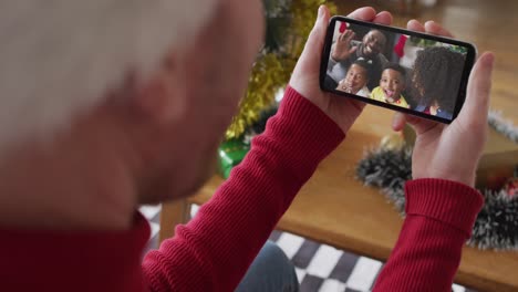 Kaukasischer-Mann-Mit-Weihnachtsmütze-Nutzt-Smartphone-Für-Weihnachtsvideoanruf-Mit-Lächelnder-Familie-Auf-Dem-Bildschirm