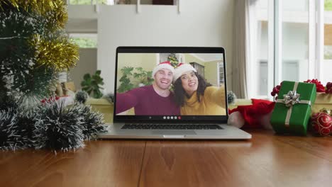 Smiling-diverse-couple-wearing-santa-hats-on-christmas-video-call-on-laptop