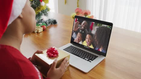 Afroamerikanische-Frau-Mit-Weihnachtsmütze-Nutzt-Laptop-Für-Weihnachtsvideoanruf,-Mit-Familie-Auf-Dem-Bildschirm