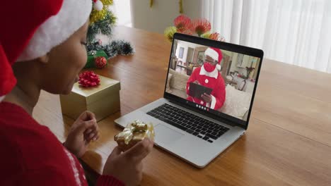 Afroamerikanische-Frau-Mit-Weihnachtsmannmütze-Nutzt-Laptop-Für-Weihnachtsvideoanruf,-Mit-Weihnachtsmann-Auf-Dem-Bildschirm
