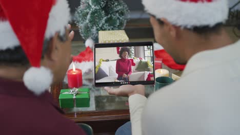 Biracial-father-and-son-waving-and-using-tablet-for-christmas-video-call-with-happy-woman-on-screen