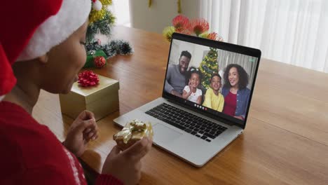 Mujer-Afroamericana-Con-Sombrero-De-Santa-Usando-Una-Computadora-Portátil-Para-Una-Videollamada-Navideña-Con-La-Familia-En-La-Pantalla
