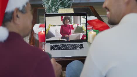 Smiling-biracial-father-and-son-using-laptop-for-christmas-video-call-with-happy-woman-on-screen