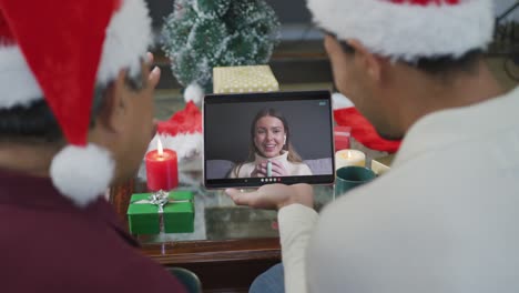 Biracial-father-with-son-waving-and-using-tablet-for-christmas-video-call-with-woman-on-screen