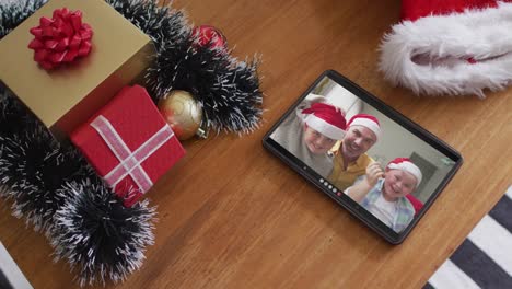 Smiling-caucasian-family-wearing-santa-hats-on-christmas-video-call-on-tablet