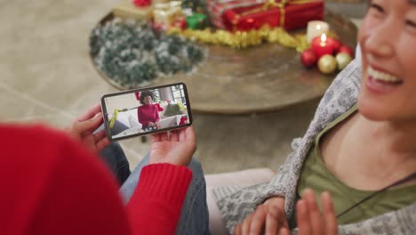 Smiling-asian-couple-using-smartphone-for-christmas-video-call-with-woman-with-santa-hat-on-screen
