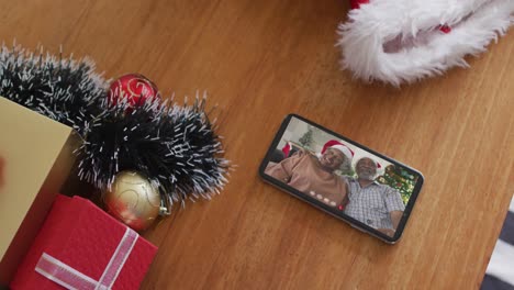 Lächelndes-älteres-Afroamerikanisches-Paar-Mit-Weihnachtsmützen-Bei-Weihnachtsvideoanruf-Auf-Dem-Smartphone
